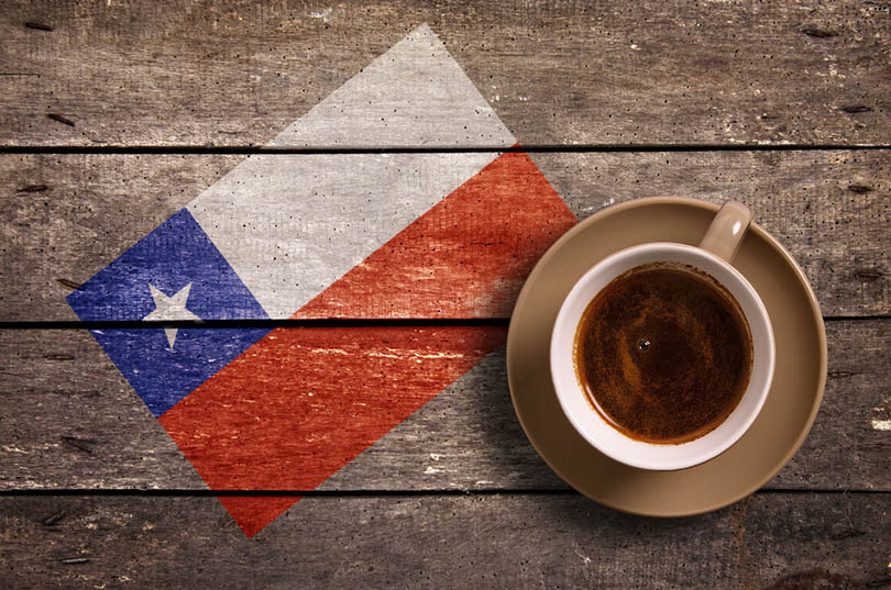 一杯咖啡在一个茶碟的在一张木桌上与智利的旗子