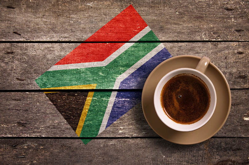 一杯咖啡在木质表面上，有南非的旗帜